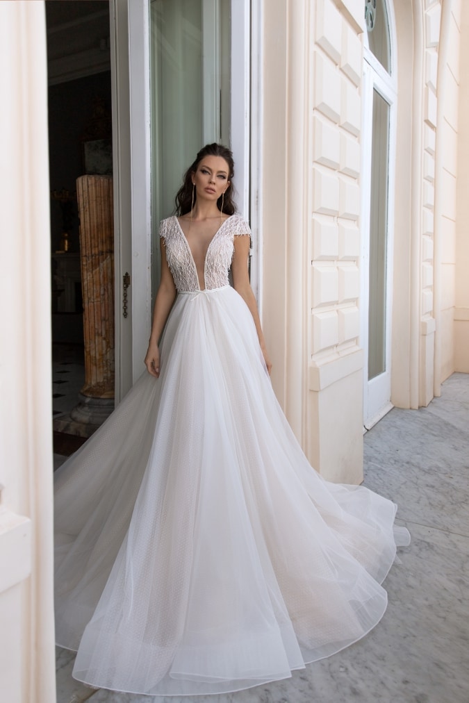 Cap sleeve ivory wedding dress with plunging neckline worn by a model