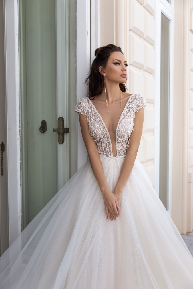 Close detail of a cap sleeve ivory wedding dress with plunging neckline worn by a model