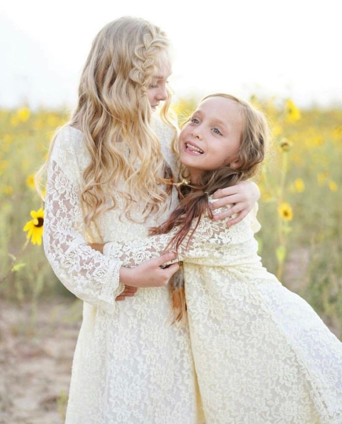 Two gilrs wearing white lace dresses and in a flower field