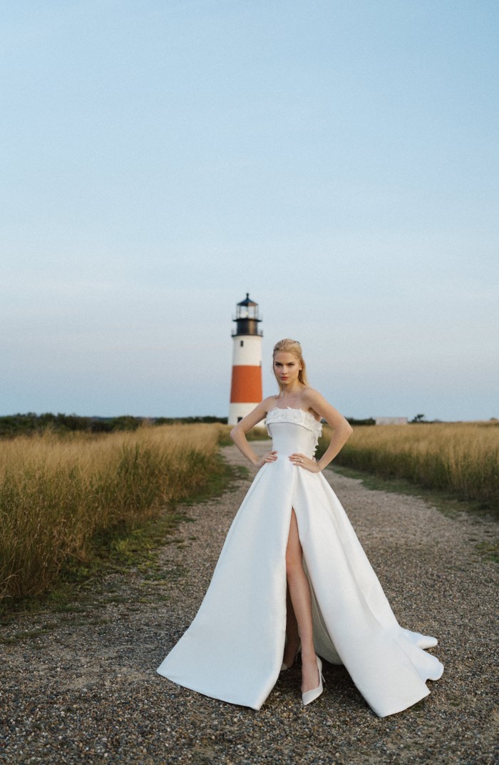 Model wearing strapless ball gown wedding dress in front of lighthouse in Nantucket.