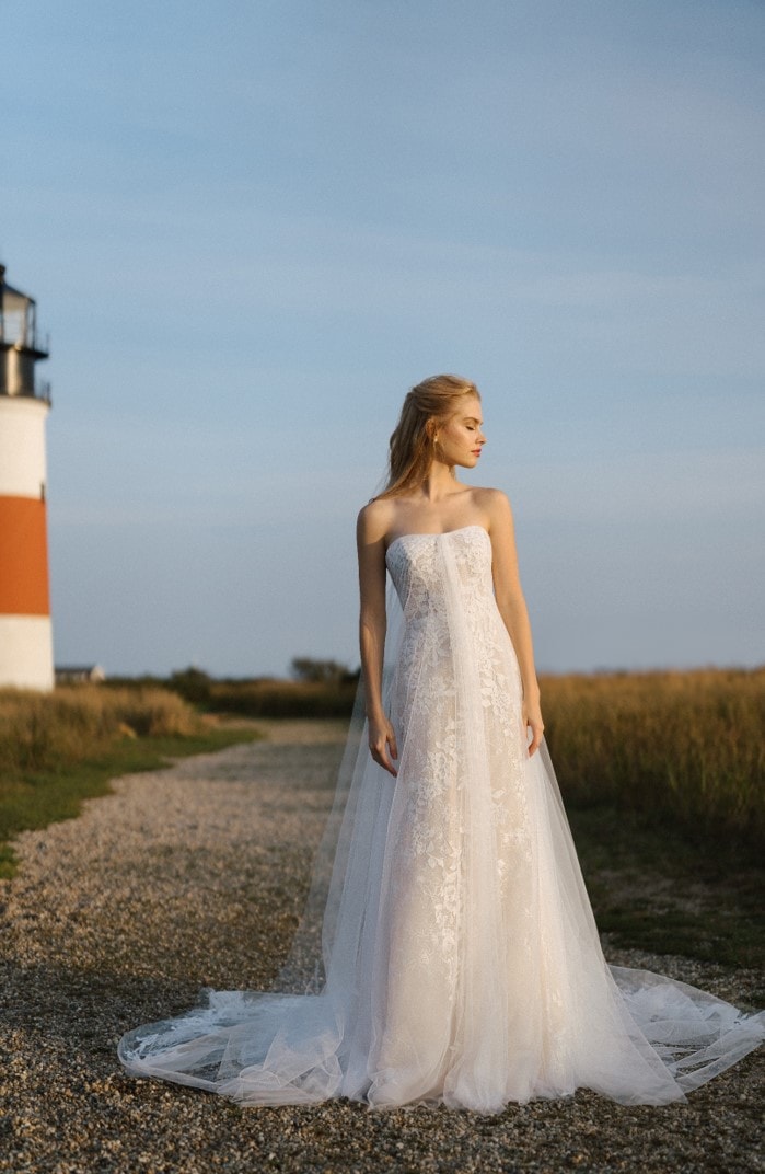 Model wearing strapless wedding dress in front of a lighthouse