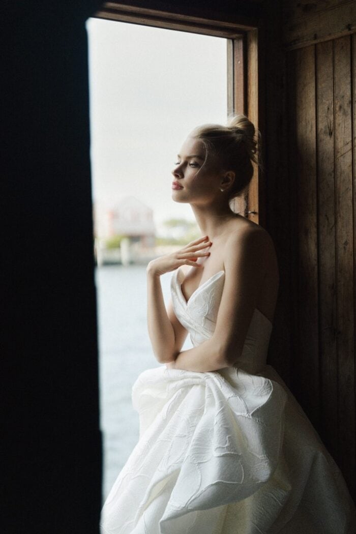 model wearing strapless ballgown wedding dress looking through window of fish shanty