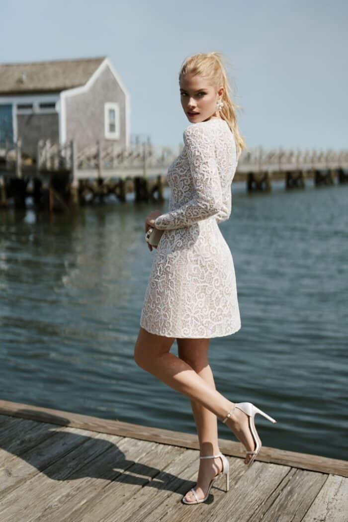 Full length image of model wearing a short lace wedding dress with long sleeves