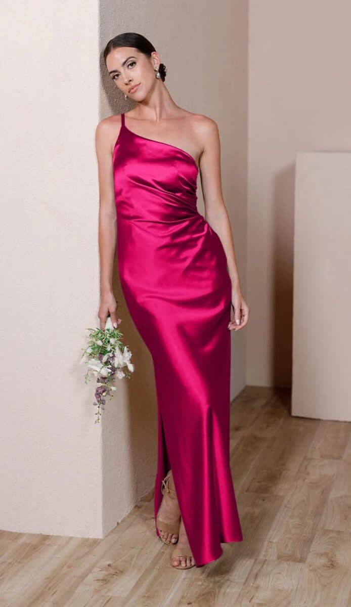 Model wearing one shoulder hot pink satin gown leaning on a wall
