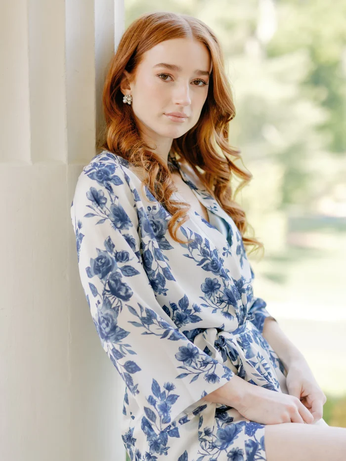 Model leaning against wall wearing a blue and white floral robe for bridesmaids
