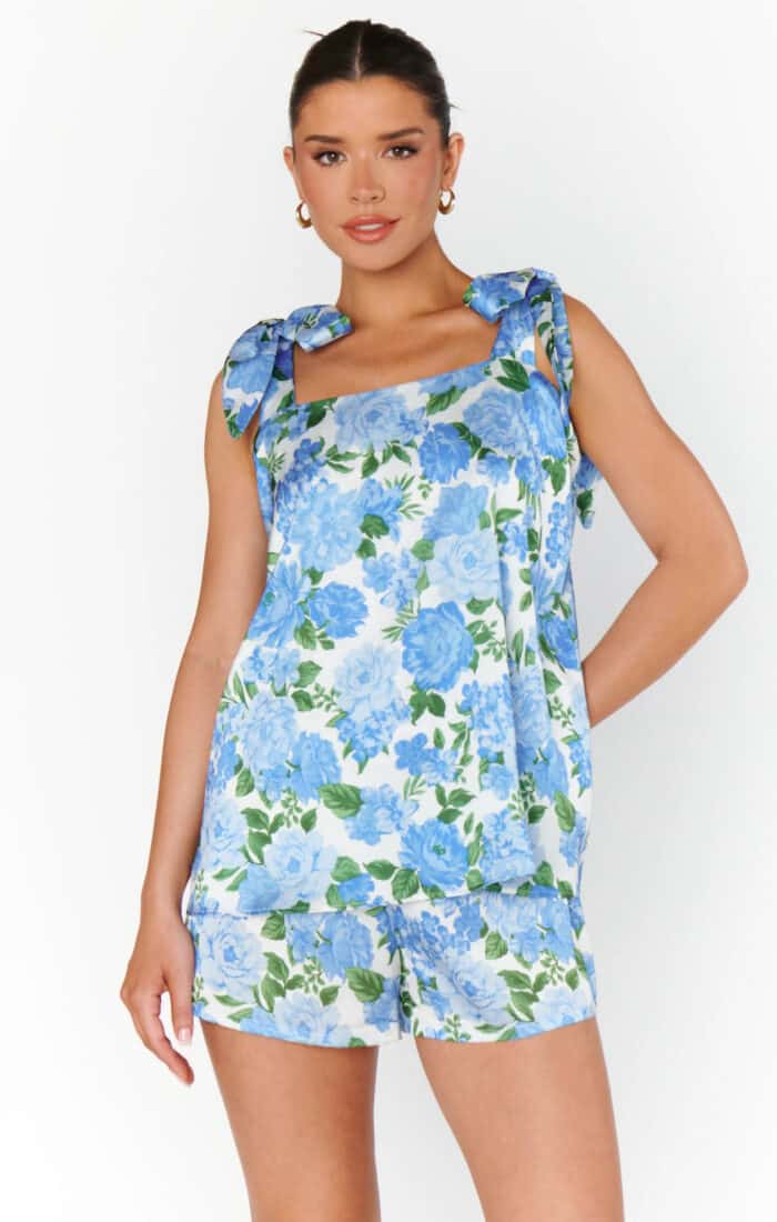 Model wearing a wide neck makeup tank with ties at the shoulder and short set with blue flower print.