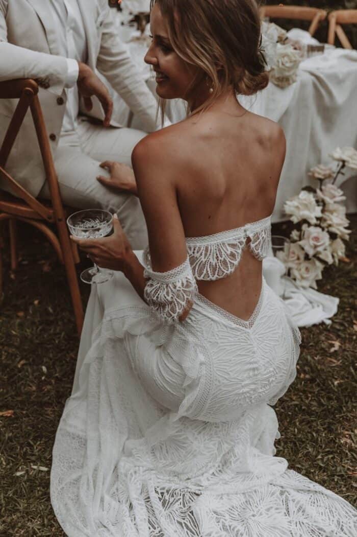 Bride shows the back detail of a lace boho style wedding dress.