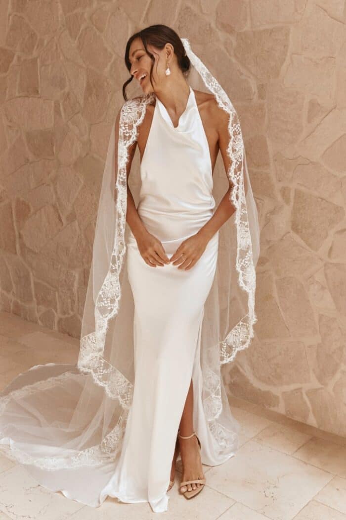 Model wearing veil and halter style sleeveless satin wedding dress.