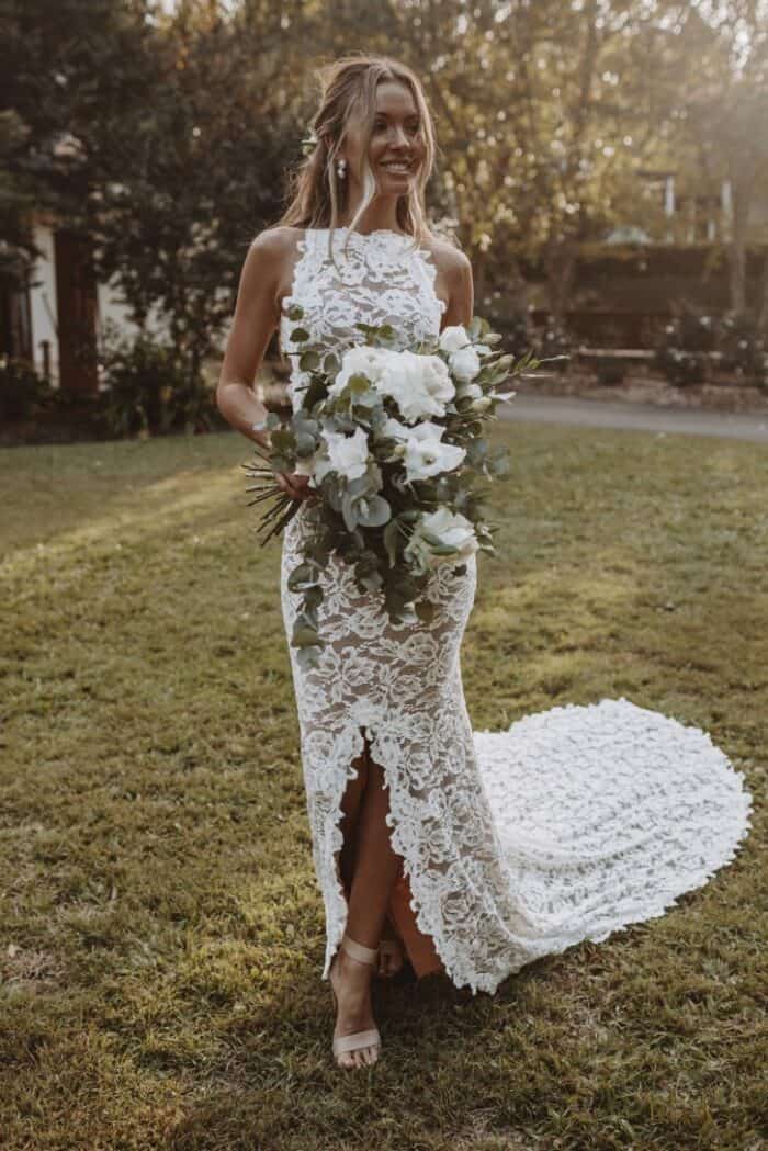 Model holiding flowers wears a high neck sleeveless lace wedding dress