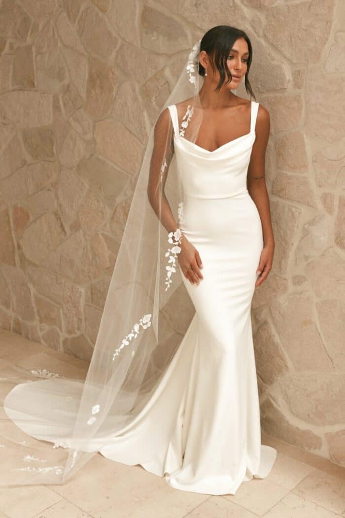 A model wears a square cowl neck crepe wedding dress with veil.