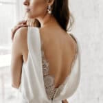 Image of a brunette model wearing a wedding dress with open lace trimmed back.